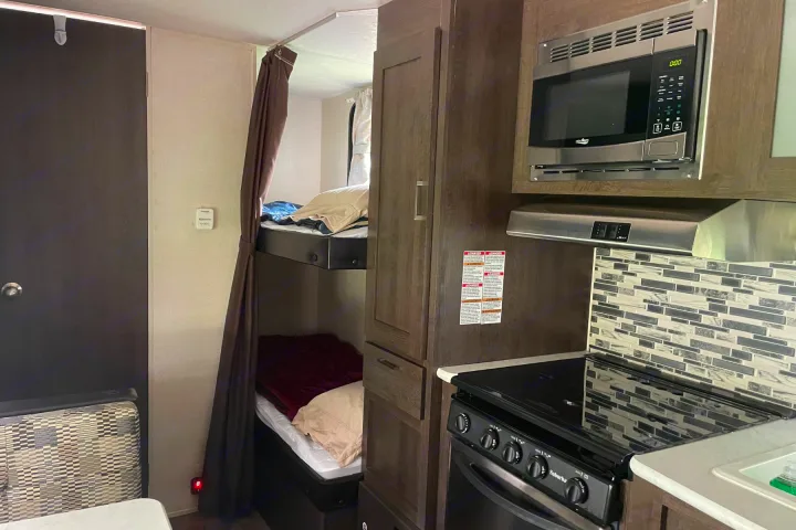 Cozy RV rental interior showcasing bunk beds with privacy curtain, a compact kitchen with microwave, and stove for comfortable travel.. Forest River Wildwood X-Lite 2018