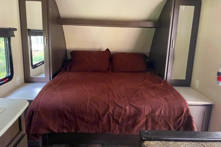This cozy RV rental bedroom features a comfortable bed with brown bedding, built-in mirrored wardrobes, and side tables, ideal for travel.. Forest River Wildwood X-Lite 2018