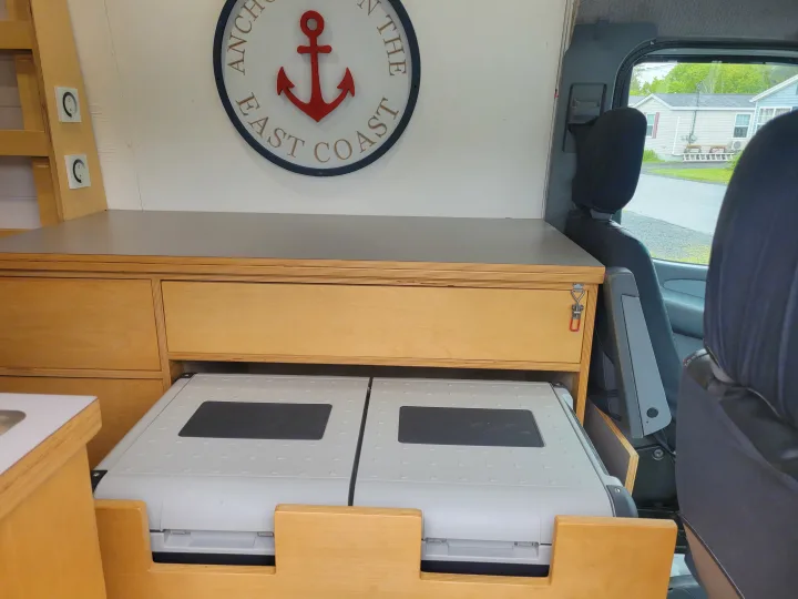 Inside an RV rental: custom wood cabinetry, pull-out chest fridges, and an 'East Coast' anchor sign in a camper van.. Mercedes Sprinter 2006