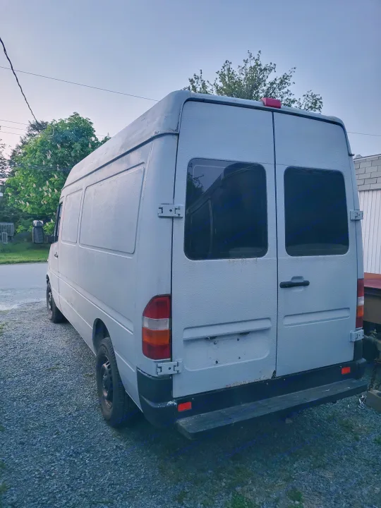 A light gray Sprinter van, possibly an RV rental, parked on gravel. Features textured paint and rear door windows.. Mercedes Sprinter 2006