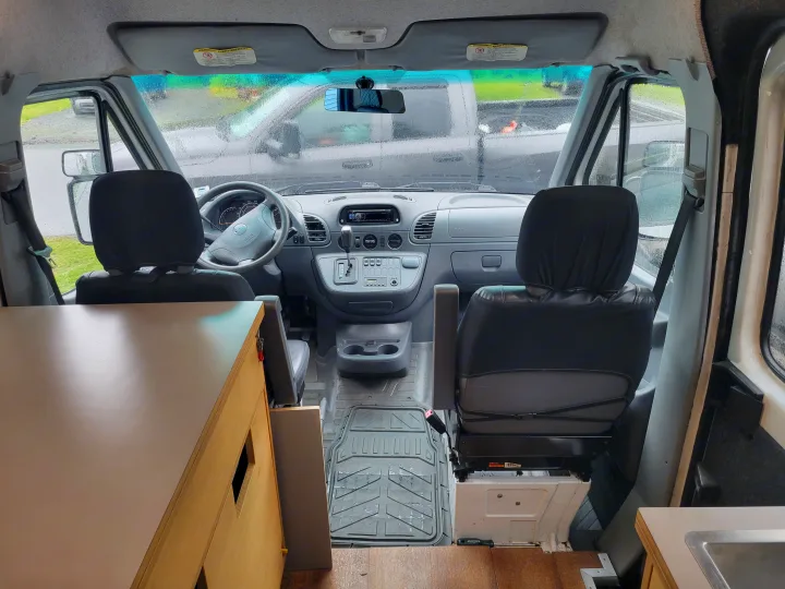 Inside a camper van or RV rental: View of the cockpit from the living area, showing front seats & dashboard.. Mercedes Sprinter 2006