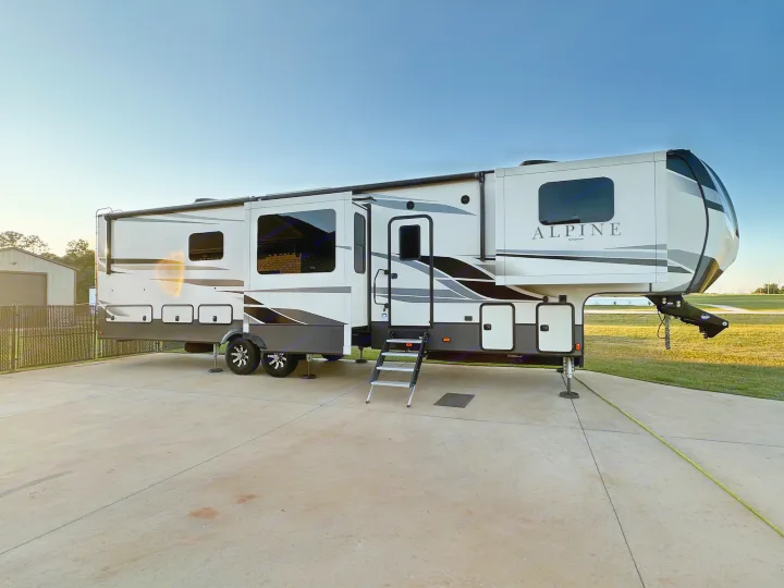 A sleek, white and grey Alpine fifth-wheel RV, ideal for your next rv rental adventure, parked on concrete with slide-outs extended.. Keystone RV Alpine 2021