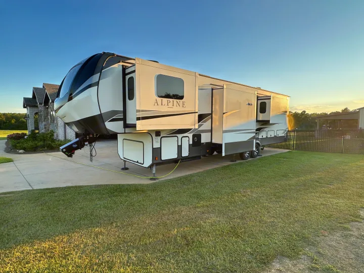 Luxury Alpine fifth-wheel RV rental with extended slide-outs, parked on a driveway. Ready for your spacious glamping adventure!. Keystone RV Alpine 2021