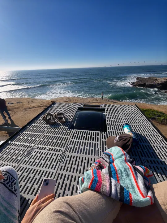 Relaxing on an RV rental rooftop deck overlooking the scenic coast. Blue skies, ocean waves, and flying birds.. Dodge Ram 1500 2021