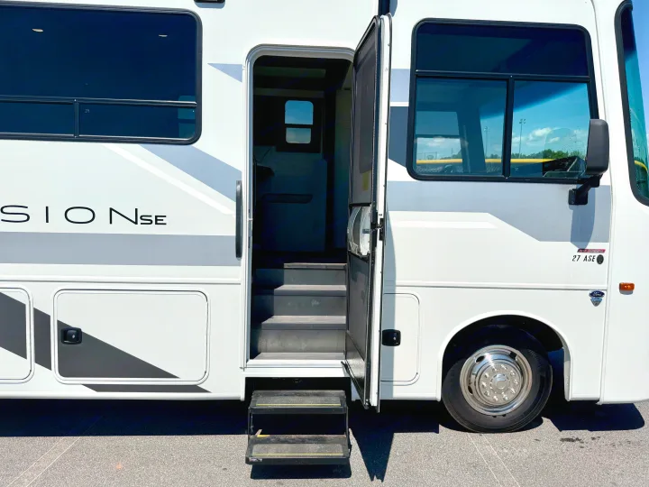Side view of a clean white RV rental, a recreational vehicle (motorhome) with its entrance door open and steps extended.. Entegra Coach Vison 27ASE 2025
