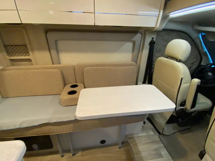 Inside an RV rental: cozy light-colored seating, removable table, overhead cabinets, and swivel front passenger seat.. Thor Rize 2023