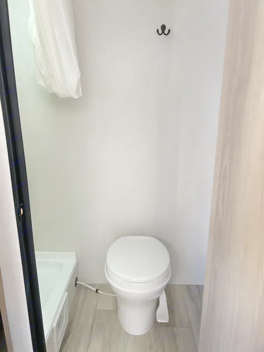 Compact RV rental bathroom features a white toilet, small shower, and wall hook for convenience.. Coleman Lantern 17B 2025