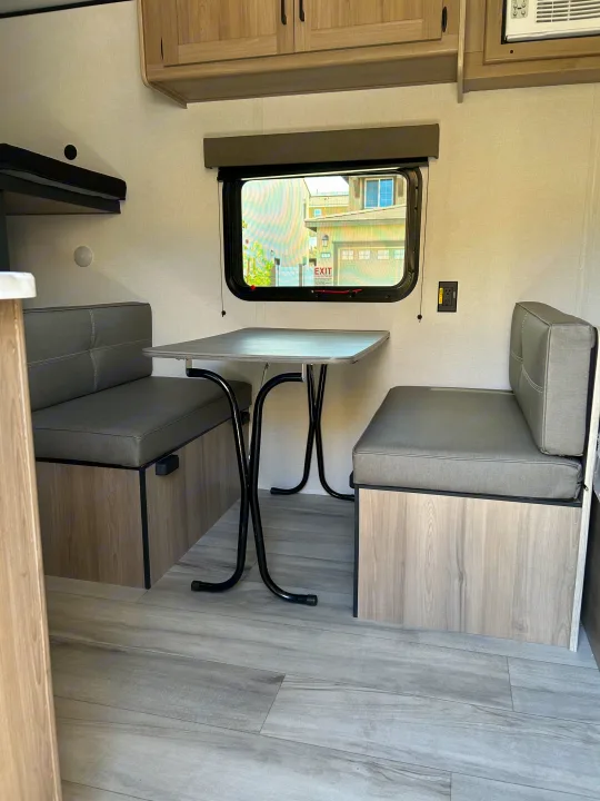 Cozy RV rental interior with a modern dinette, two benches, table, and window view. Perfect for road trip adventures.. Coleman Lantern 17B 2025