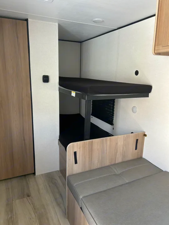 This RV rental shows a clean interior with bunk beds, a wood-look wardrobe, and gray dinette seating. Perfect for your travels.. Coleman Lantern 17B 2025