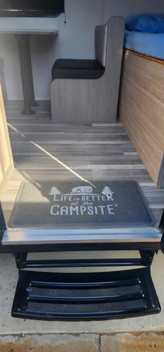 RV rental interior: dinette, bed, wood floor, "Campsite" entry mat, and outdoor steps.. Heartland Pioneer 2025