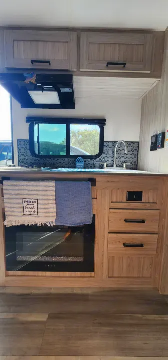 Compact RV rental kitchen with modern wood cabinets, stovetop, sink, microwave, and electric fireplace, perfect for travel.. Heartland Pioneer 2025