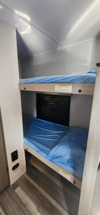 Bunk beds in an rv rental, made with light blue sheets. A 200 lbs max load caution sticker is on the upper bunk frame.. Heartland Pioneer 2025