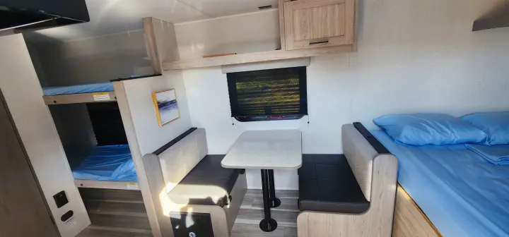 RV rental's inviting interior: bunk beds, a dinette table with benches, and a main bed with blue linen.. Heartland Pioneer 2025