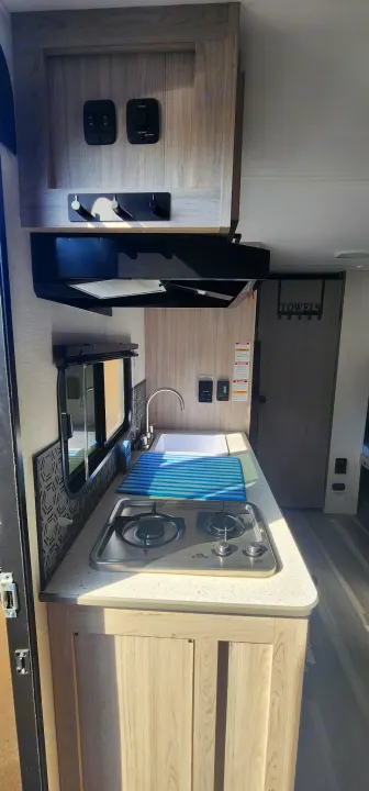 Inside an RV rental: Compact kitchen with a two-burner stovetop, sink, microwave, and essential controls for your adventure.. Heartland Pioneer 2025