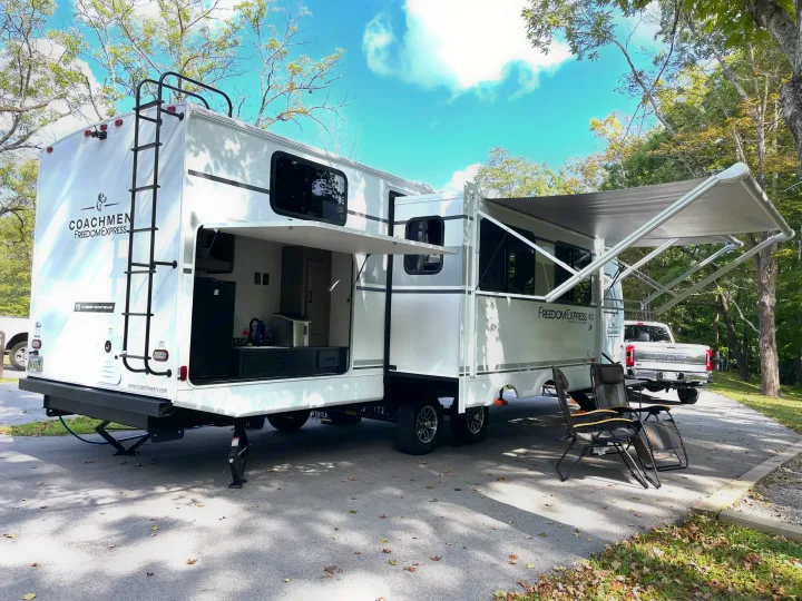 Spacious Coachmen Freedom Express travel trailer RV rental at a campsite, featuring an extended awning & outdoor kitchen.. Coachmen Freedom Express Ultra Lite 2025