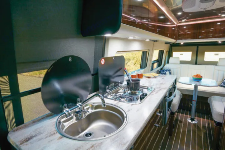 Inside a stylish rv rental: a compact kitchen with sink, stove, and a cozy dining area with white seating.. Airstream Interstate 2017