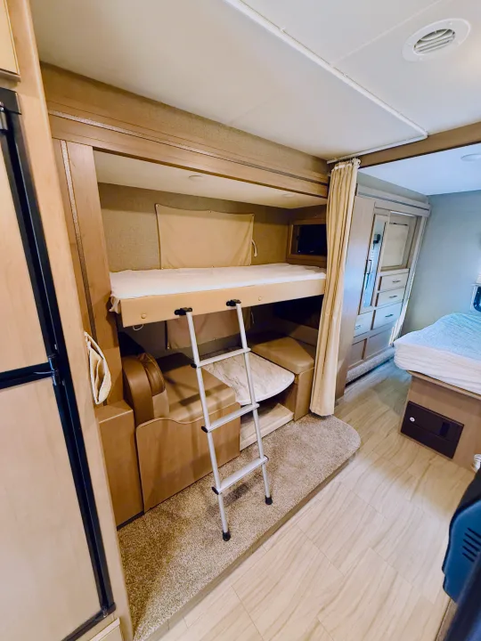 Inside an RV rental: cozy bunk beds with ladder, compact dinette, and main bed, optimized for family comfort.. Thor Coleman 2021