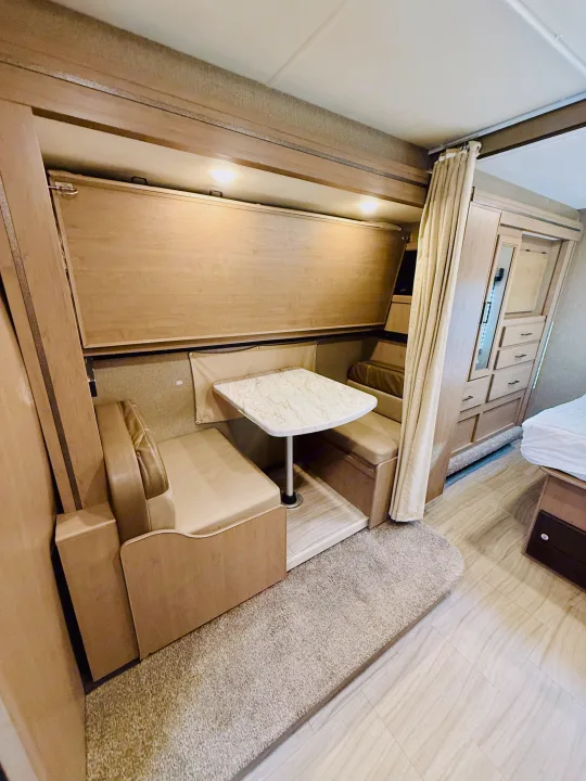 RV rental interior: a cozy dinette with a fold-up bunk bed above, plus ample cabinetry and a main bed visible. Ideal for travel.. Thor Coleman 2021