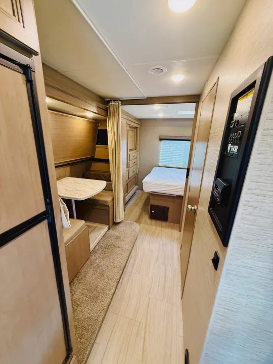 Step inside this inviting RV rental. The compact interior features a dinette, refrigerator, and a cozy bedroom with controls visible on the wall.. Thor Coleman 2021
