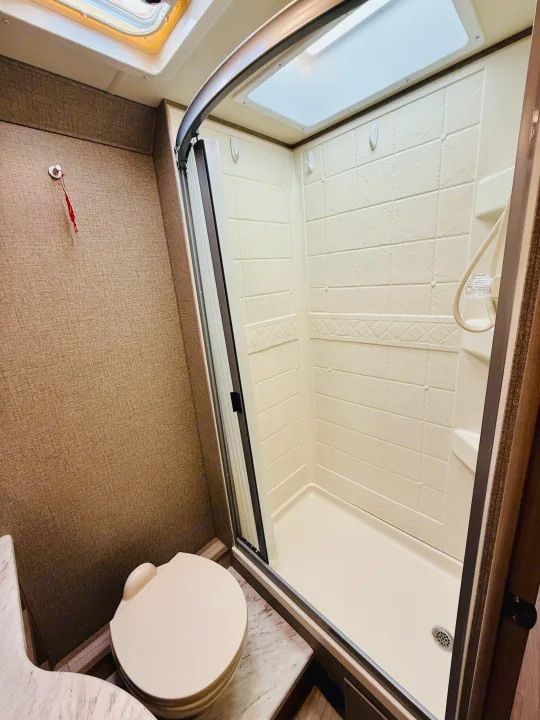This RV rental features a compact, clean bathroom with a toilet and a bright shower stall, complete with a skylight.. Thor Coleman 2021