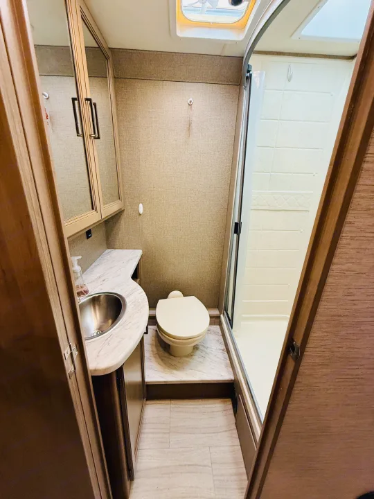 Compact RV rental bathroom with a vanity, toilet, and shower stall, designed for efficient use.. Thor Coleman 2021