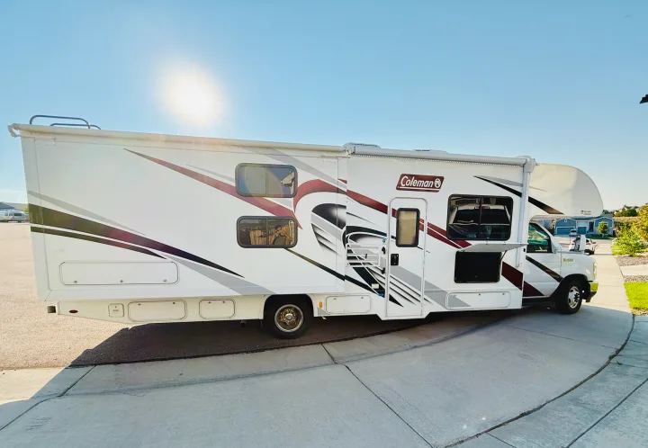 White Coleman RV rental parked on a sunny concrete driveway. This motorhome features distinctive modern graphics.. Thor Coleman 2021