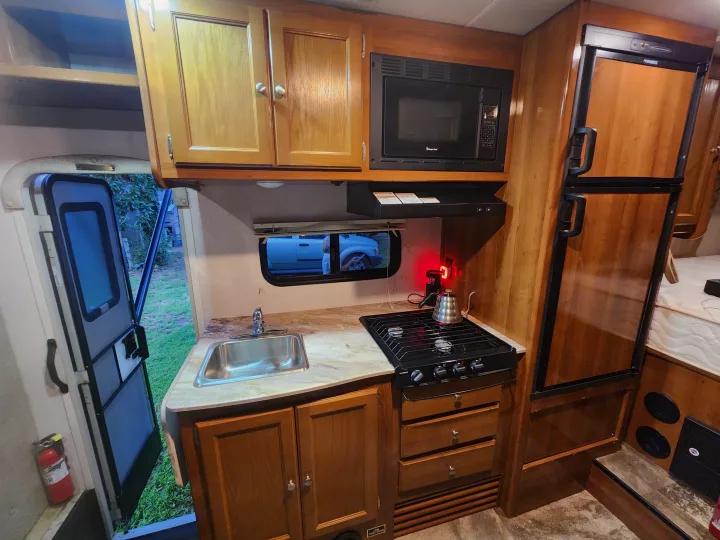 RV rental kitchen featuring stove, microwave, fridge, sink, and cabinets for your adventures.. Coachmen Leprechaun 220QB 2019