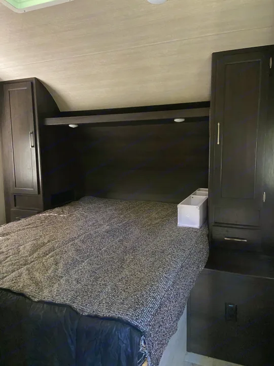 Cozy RV rental bedroom with a comfy bed, dark wood cabinets, and overhead storage, offering a functional sleeping area.. Genesis Supreme Rv Genesis Supreme 2022