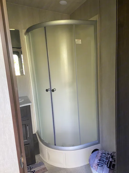 Compact frosted glass corner shower in an RV rental bathroom, with a vanity and partially visible toilet.. Genesis Supreme Rv Genesis Supreme 2022