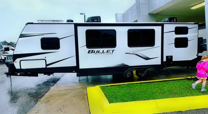 Keystone Bullet Ultra Lite travel trailer RV rental. Parked on wet pavement, a child in pink passes by.. Keystone RV Bullet Ultra Lite 2022