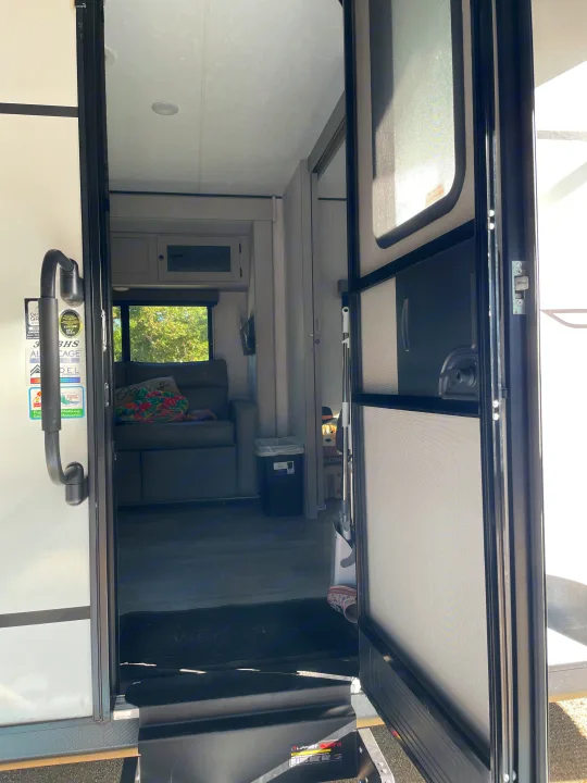 Welcome to your next adventure! The open doorway of an RV rental shows a comfortable living area & outdoor view.. Coachmen Apex 300 BHS 2025