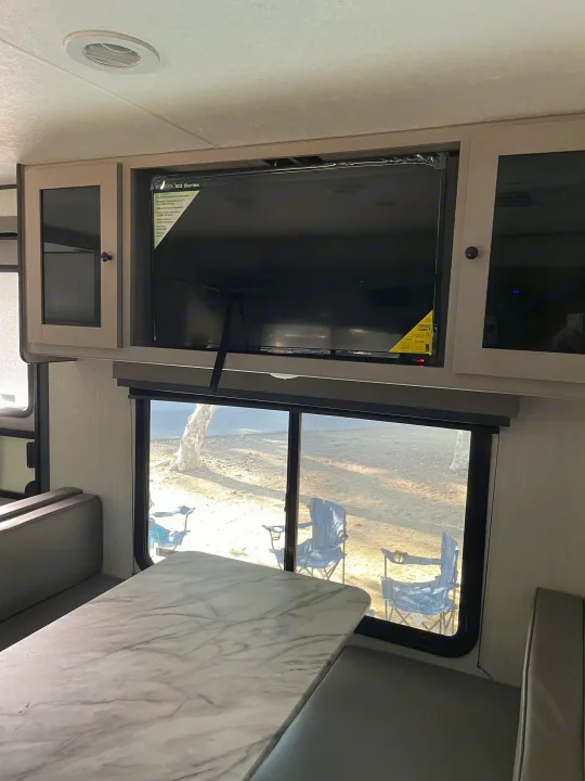 RV rental interior showcasing a dining area with a TV, bench seating, and windows overlooking an outdoor campsite.. Coachmen Apex 300 BHS 2025