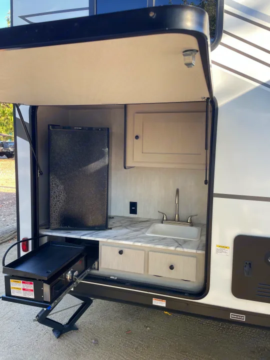 This RV rental features a convenient outdoor kitchen with a black fridge, sink, and pull-out griddle setup.. Coachmen Apex 300 BHS 2025