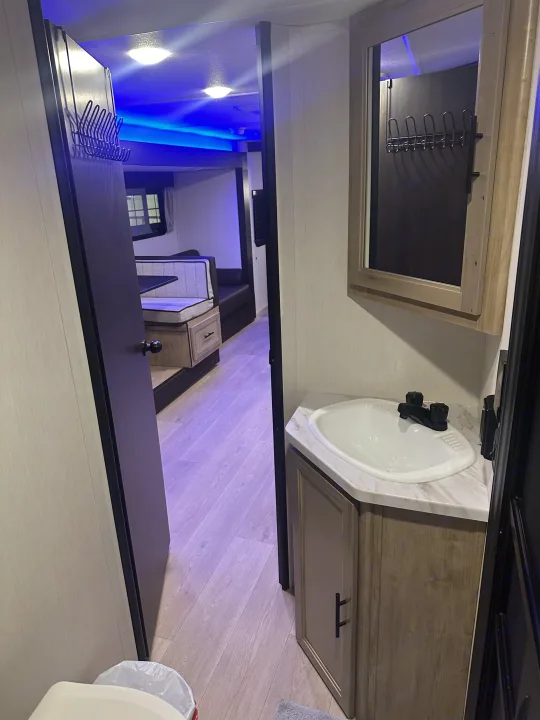An RV rental interior featuring a compact bathroom sink area, with a doorway leading to the dinette and blue accent lights.. Forest River Cherokee Grey Wolf 2026