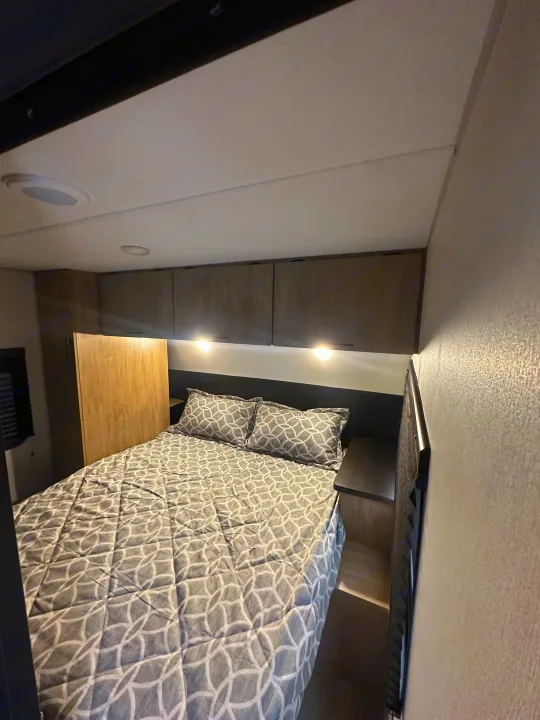 Explore a comfy RV rental travel trailer bedroom with a patterned bed, storage cabinets, and ambient lighting.. Forest River Cherokee Grey Wolf 2026