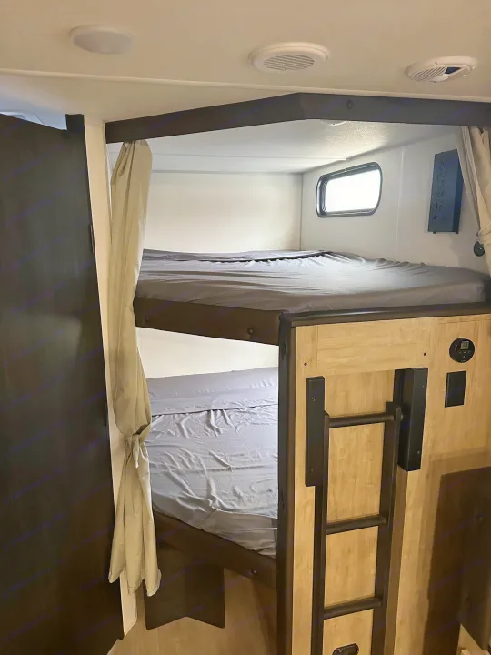 RV rental interior: two clean bunk beds with grey sheets, a ladder, and overhead vents visible.. Forest River Cherokee Grey Wolf 2026