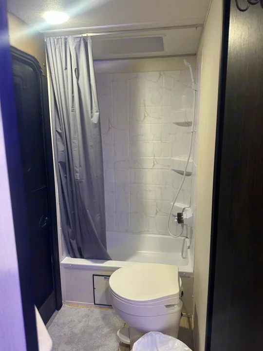 RV rental bathroom features a clean shower-tub combo with a gray curtain, toilet, and light-colored interior.. Forest River Cherokee Grey Wolf 2026