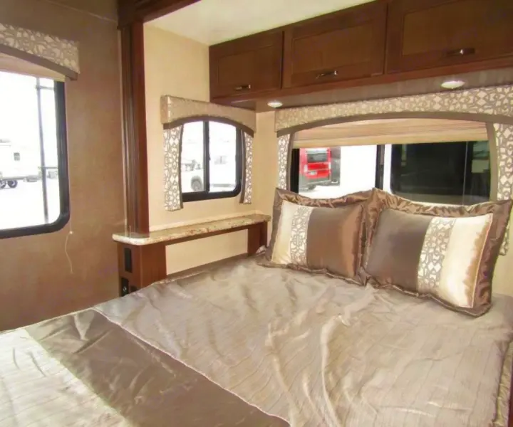 RV rental interior: a comfy bedroom featuring a bed with decorative pillows, ample overhead cabinets, and bright windows.. Thor Chateau 2019