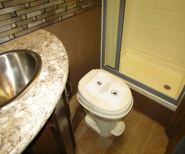 Inside an RV rental bathroom: a sink, toilet with a paper on its lid, and a standing shower.. Thor Chateau 2019