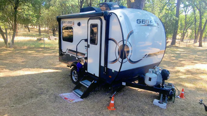 White Geo Pro travel trailer rv rental, with steps down and propane tanks, parked on grass among trees.. Forest River Rockwood Geo Pro 2024