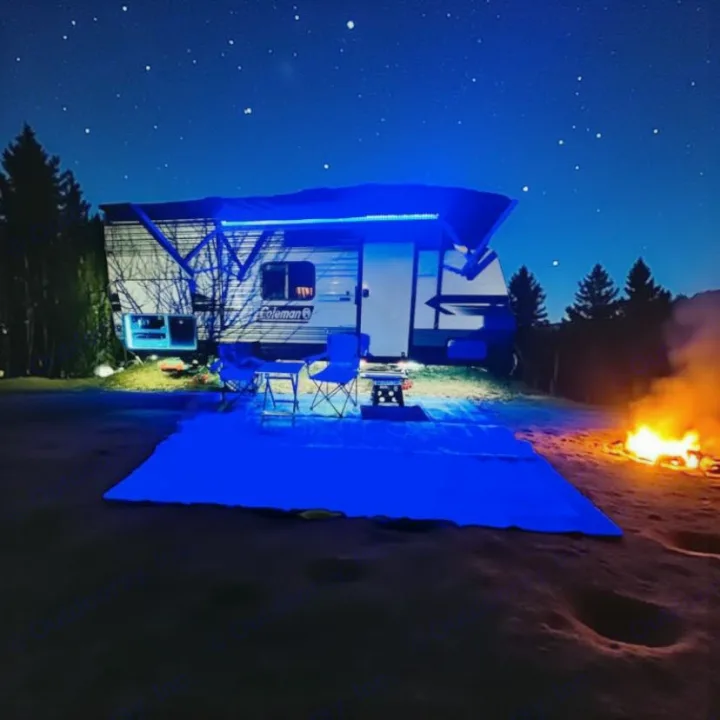 A vibrant RV rental illuminated by blue lights, with a roaring campfire nearby under a clear, starry night sky.. Dutchmen Coleman Lantern LT 2022