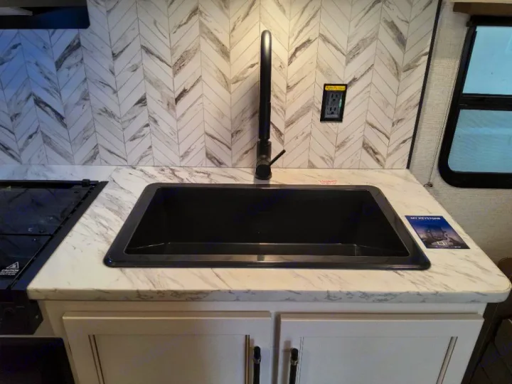 This RV rental kitchen features a sleek black sink, marbled counter, and chevron backsplash, with a modern faucet.. Keystone Springdale Classic 2025