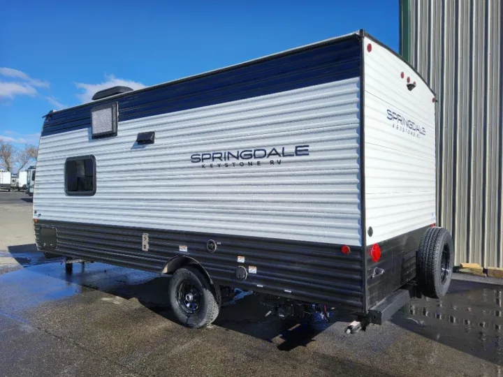 White and black Springdale Keystone travel trailer, perfect for an RV rental. View shows the side and rear with a spare tire.. Keystone Springdale Classic Mini 2025