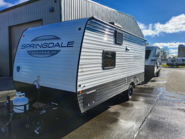 A white and black Springdale Keystone RV travel trailer, with a propane tank, ready for an rv rental. Parked on wet pavement.. Keystone Springdale Classic Mini 2025