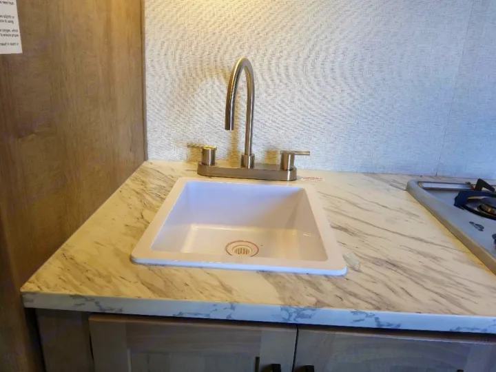 This rv rental features a compact kitchen with a white sink, chrome faucet, and marbled countertop.. Keystone Springdale Classic Mini 2025