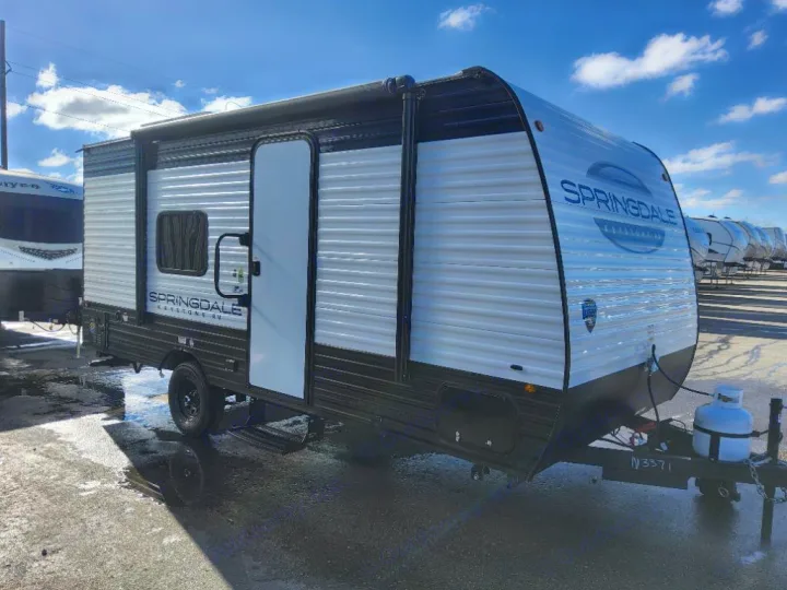 This Keystone Springdale travel trailer, ideal for an RV rental, features a sleek white and black exterior parked on a wet lot.. Keystone Springdale Classic Mini 2025