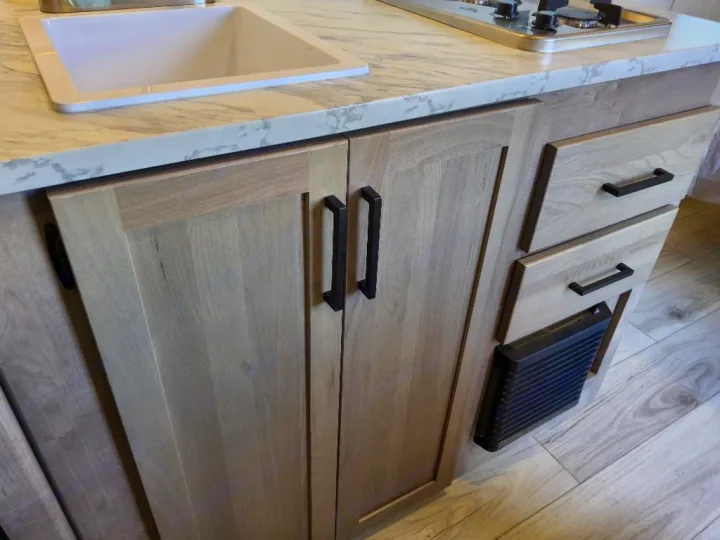 Inside an RV rental: a modern kitchen galley with light wood cabinets, black handles, a white sink, and marbled countertop.. Keystone Springdale Classic Mini 2025