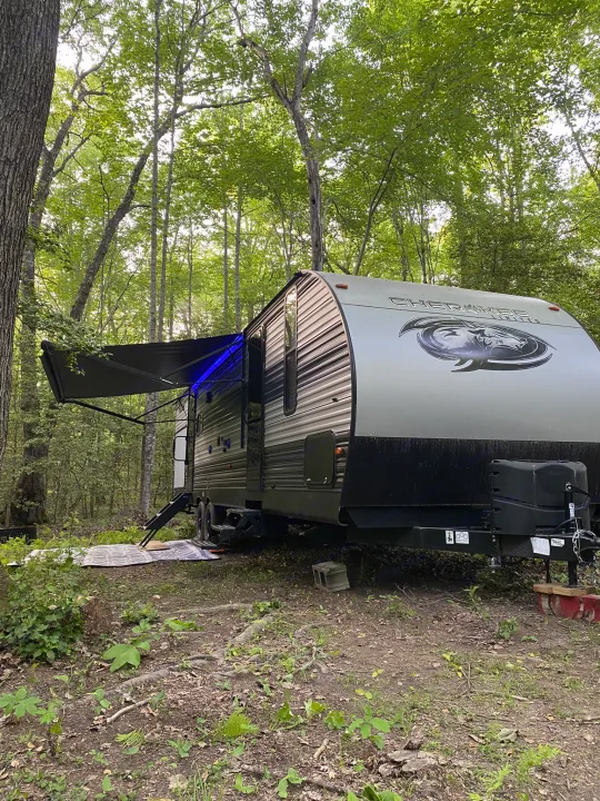Cherokee travel trailer rv rental set up in a shaded forest campsite, its awning extended with blue LED lights.. Forest River Cherokee 2021