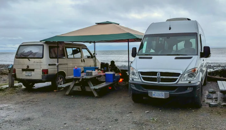 Serene beach camping: Two camper vans, including an RV rental, set up with a picnic and campfire by the ocean.. Mercedes Sprinter 2008