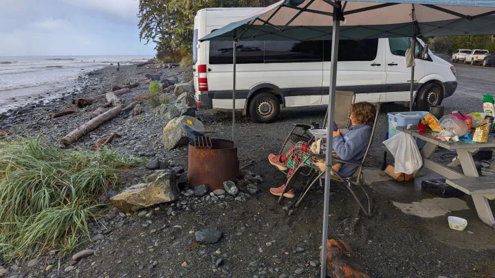 Relaxing by an RV rental on a rocky beach with a fire pit and picnic setup, perfect for coastal camping.. Mercedes Sprinter 2008